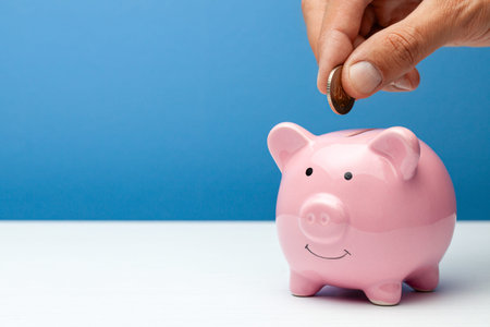 Pink piggy bank and coin in a male hand on a blue background. Copy space for text