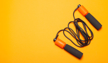 Jump rope. Fun exercises for body health. Orange rope with black cord. Yellow orange background.