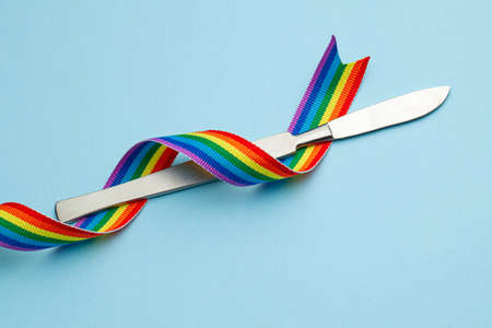Scalpel and rainbow LGBT ribbon pride symbol. Sex change operation. Blue background.の写真素材