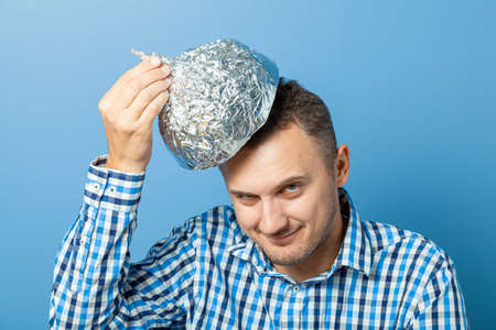 Man puts on a helmet made of aluminum foil with pleased face.. Protects from reading thinkの写真素材