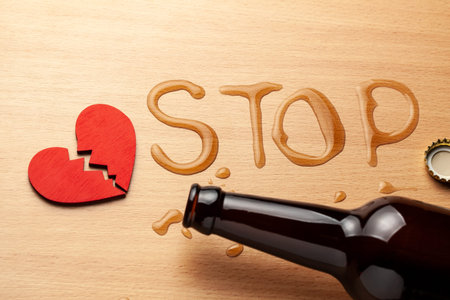 Alcoholism in the family. Broken heart, broken relationship. Beer bottle and spilled beer in the word STOP and heart with a crackの写真素材