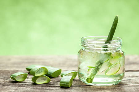 Aloe Vera gel cream for skin and body care. Aloe pulp slices in a glass jar and leaves on a wooden table. Cosmetic lotion.の写真素材
