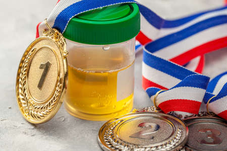 Doping test. Gold, silver and bronze medal and a jar for urine analysis on a gray backgroundの写真素材