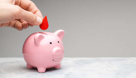 Blood donor. A man holds a red drop of blood in his hand and puts it in a piggy bank as a donationの写真素材
