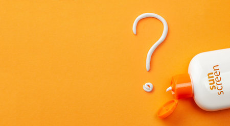 Sunscreen on orange background. Plastic bottle of sun protection and white cream in the form of...