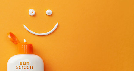 Sunscreen on orange background. Plastic bottle of sun protection and white cream in the shape of...