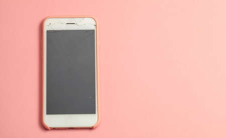 Broken phone with crack on the display glass on pink background. Copy space for text.の写真素材