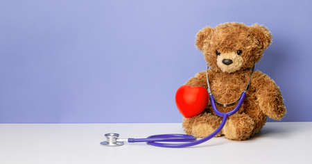 Teddy bear with a stethoscope and a heart on a purple background. Family doctor or pediatrician concept. Template Copy space for textの写真素材