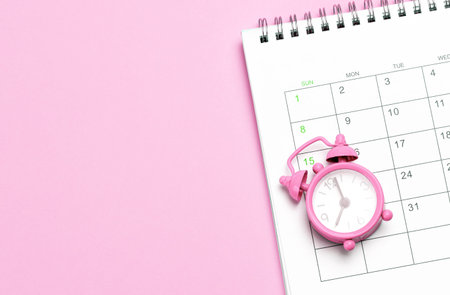 Pink alarm clock and calendar on a pink background. Concept days of menstruation or menopause....