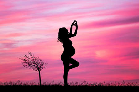 a pregnant woman doing yoga at sunsetの写真素材