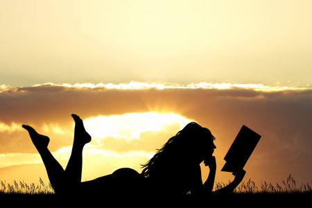 girl lying on the grass reads a book at sunsetの写真素材