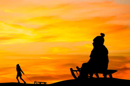 people with sleds play in the snow at sunsetの写真素材