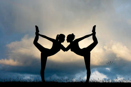 two girls do yoga at sunsetの写真素材