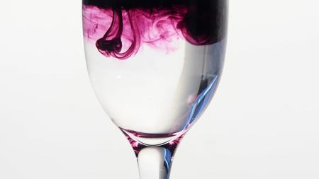 Purple ink dropping into glass of plain water.の写真素材