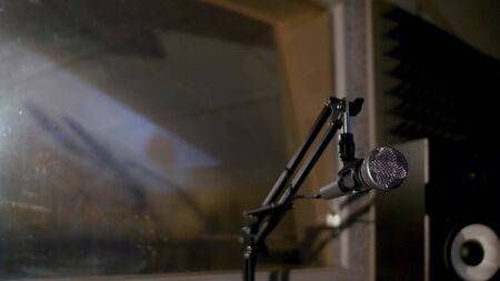 Microphone on a stand located in a music studio recording booth under low key light.の写真素材