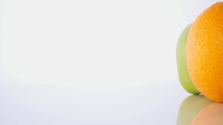 An orange and a green apple. The fruit is rotating slowly on a white background.の写真素材