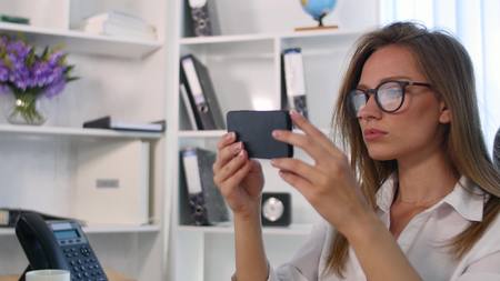 Office woman fixing her hair using smartphone as a mirror.の写真素材