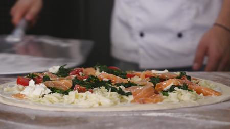 Tracking closeup shot of placing unbaked pizza with toppings from floury table on metal peel.の写真素材