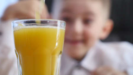 orange juice pouring into glass. little boy background. selective focus.の写真素材