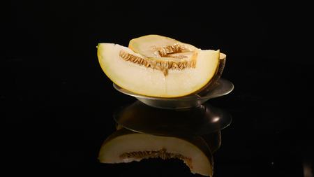 A bright juicy melon. A half of a ripe pulp rotate on a black background. Cut melon. Natural and organic ingredients.の写真素材