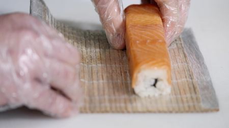 Close-up of chef hands preparing japanese food making sushi at restaurant. Young cook serving traditional modern japan meal in industrial kitchen. Close up shooting of arms of cook-chef making rolls.の写真素材