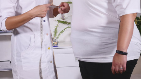 the nutritionist measures a waist of the client and writes down indicators in a notebook.
