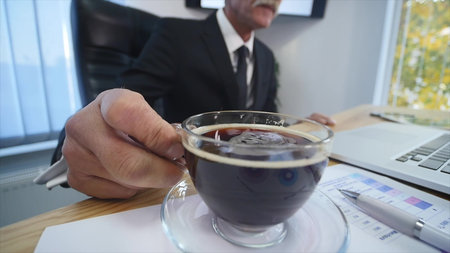 Businessman drinks coffe while watching the laptop screen.の写真素材