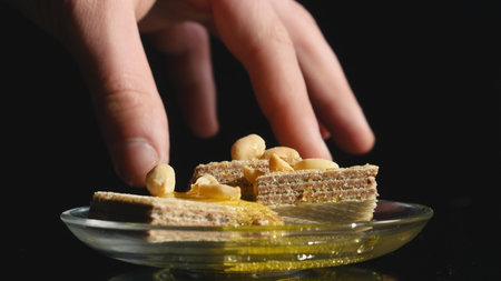 hand takes waffles with honey and nuts in a bowl on a black background.の写真素材