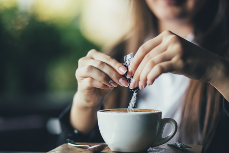 Woman adding sugar to fresh aromatic coffee on table, closeup.の写真素材