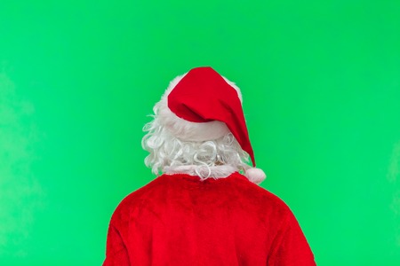 Merry Christmas. Santa Claus in a red suit is standing with his back and is looking forward on a green screen background chroma keyの写真素材
