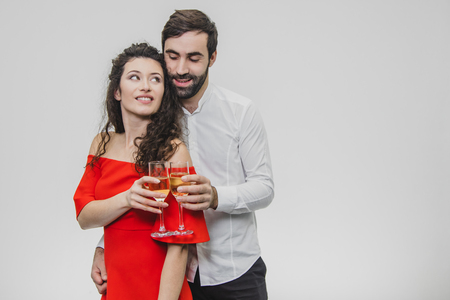 Loving young couple drinks champagne. On a white background. Dressed in red dress and white shirt.の写真素材