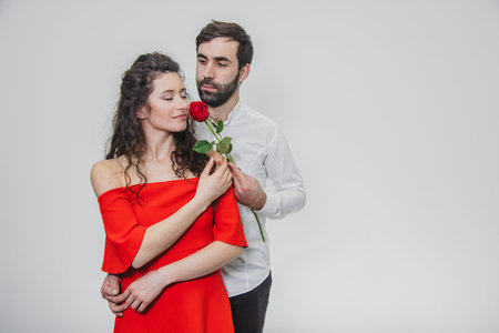 A young, handsome man gently covers his beautiful wife. During this time, one red rose.の写真素材