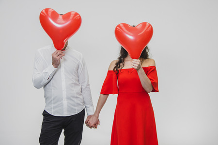 Beautiful romantic couple isolated on white background. Attractive young woman and man close balloons face. Heart-shaped balls. Valentine's Dayの写真素材