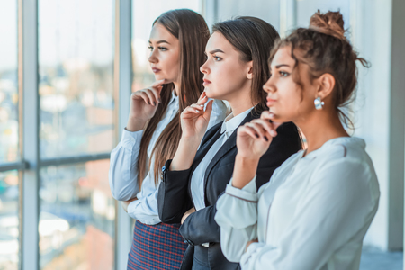 Three young beautiful brunette business ladies in the office. All serious, folded hands look to the side withの写真素材