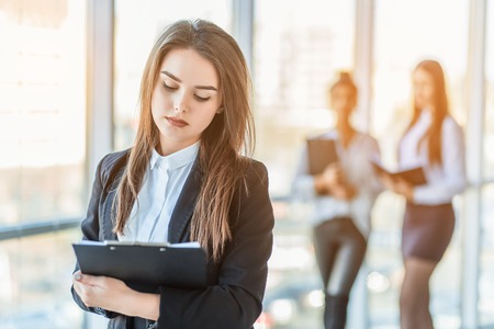 Beautiful brunette business woman in white suit with folder of documents in her hands outdoors. copy spaceの写真素材