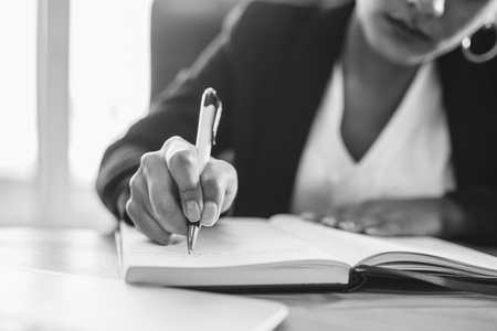 Young pretty smart business girl works in the office. During this, it creates important steps for company growth. Writing in a notebook. Black and whiteの写真素材