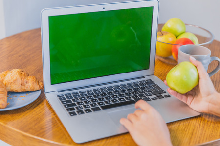Cropped snapshot of feminine hands with disposable cups of coffee and croissants. Laptop and accessories on the table. Green screenの写真素材