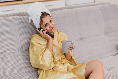 A happy woman with a remote control, choosing a television channel raises the remote control to the ears of talking. During the rest after the bath.の写真素材