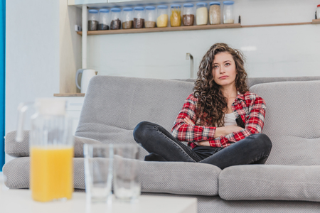 The young spectator wife watches the TV at home. During this time, sitting on the couch in the living room.の写真素材