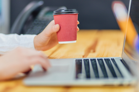 Holding a coffee young business girl working for a laptop. Lifestyle from a modern business woman using a laptop. Women's hands are working on reading an online website. Business Concept.の写真素材