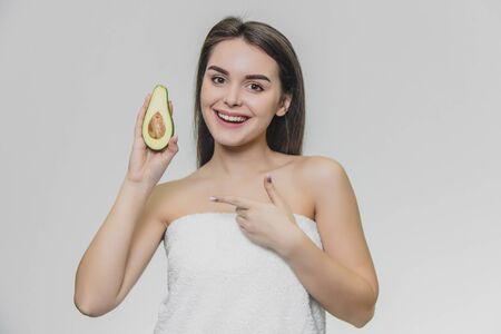 Young beautiful girl in white towel. She smiles and holds avocado in her hand.の写真素材