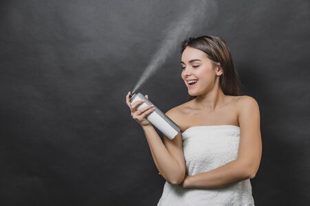 Young beautiful woman spraying hairspray isolated on black background. Head and shoulders, studio, indoors.の写真素材