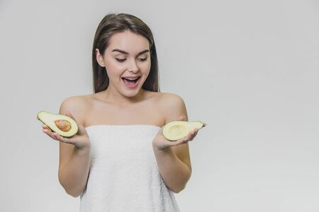 Portrait of young female woman with clean pure skin holding of avocado in hands. Astonished face. Looking down.の写真素材