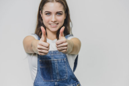 The smile of a smiling brunette in a dark blue denim overalls and a white T-shirt over a gray...