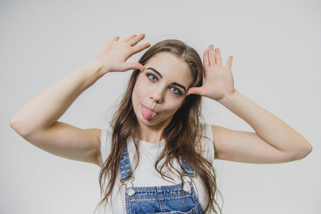 Satisfied beautiful young girl with long hair standing on a white background. Has an intriguing...