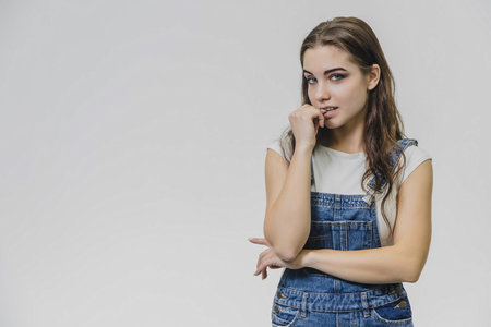 Sweet beautiful blond woman with very long hair in blue jeans overalls and glasses over grey...