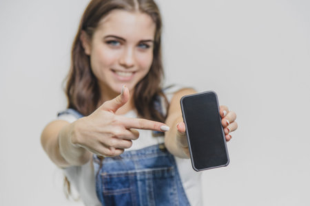 Young pretty girl standing on a white background. Shocked beautiful girl in denim overalls. Looking...