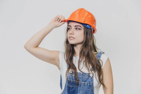 A young beautiful girl stands on a gray background. It is dressed in an orange helmet on the head. During this, he looks aside.の写真素材