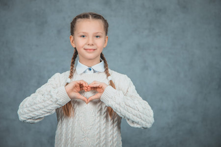 Young beautiful smart student girl shows heart and is isolated on grey background
