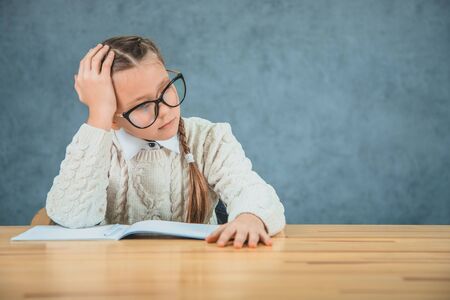 Little schoolgirl is not looking in her study materials. Girl is dreaming about something else.の写真素材